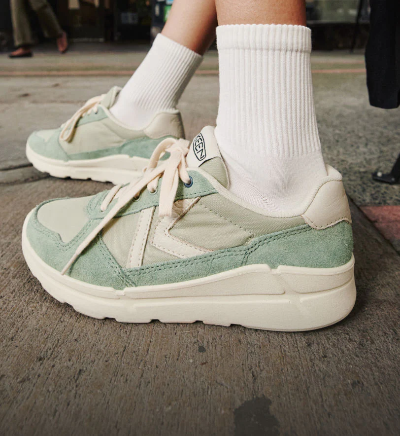 Knee-down shot of woman wearing Km1 jogger sneakers in light teal and tan.